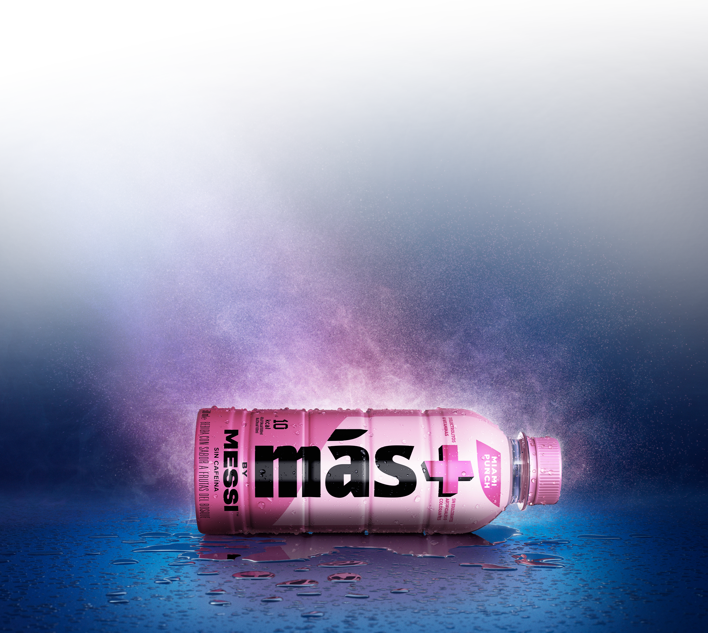 Botella rosa de la bebida funcional Más+ by Messi colocada de lado sobre el suelo con gotas de agua y un fondo brillante.